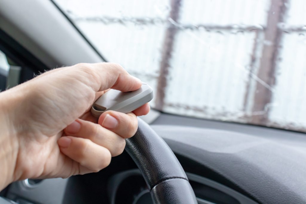 Hand inside vehicle with garage door remote control pressing to open garage door